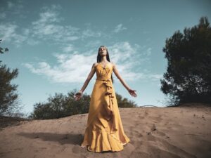 woman in yellow dress standing on brown sand under blue sky during daytime